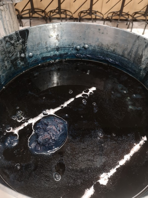 Looking down into a steel vat of reduced indigo, with the coppery purple bloom and blue-green oxidising film at the surface.