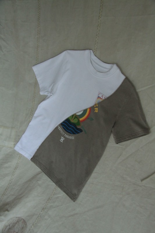 A T-shirt spliced on a long diagonal, white jersey against washed olive that keeps part of a printed sun and wave graphic.