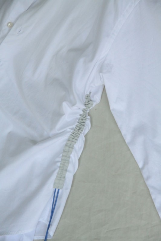 Close view of a white shirt where an elasticated shirring channel gathers the side seam, bound in pale green tape.