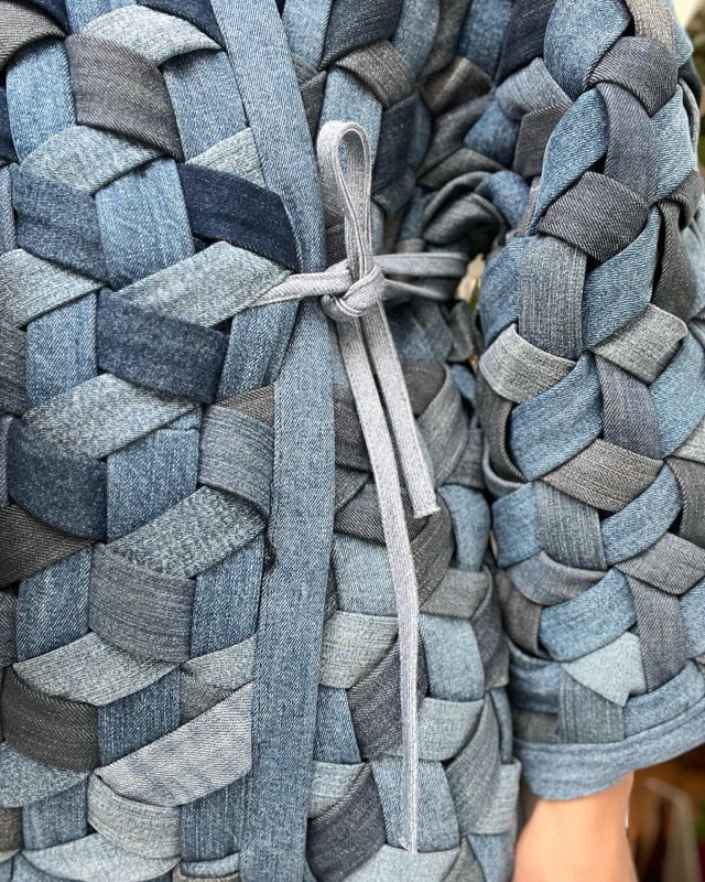 Close view of the woven denim jacket worn, showing the plaited strips and a grey jersey tie belt knotted at the front.