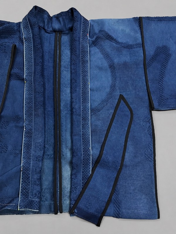 A digitally generated indigo jacket flat-lay with black bias bound front bands and a belt laid across the skirt.
