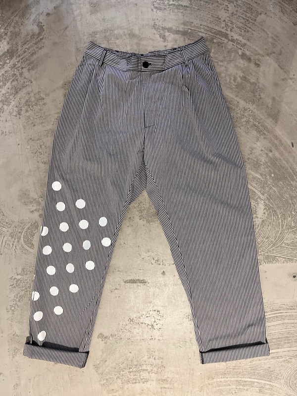 Navy and white engineer-striped trousers laid flat on concrete, with white dots printed densest at the knee.