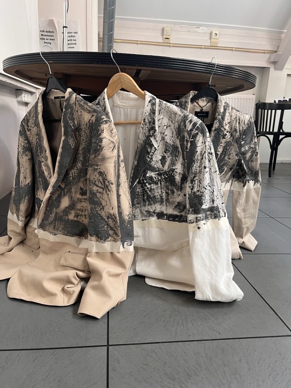 Four looks on a round hanging rail: sand canvas blousons mottled in charcoal over wide cream and beige trousers.
