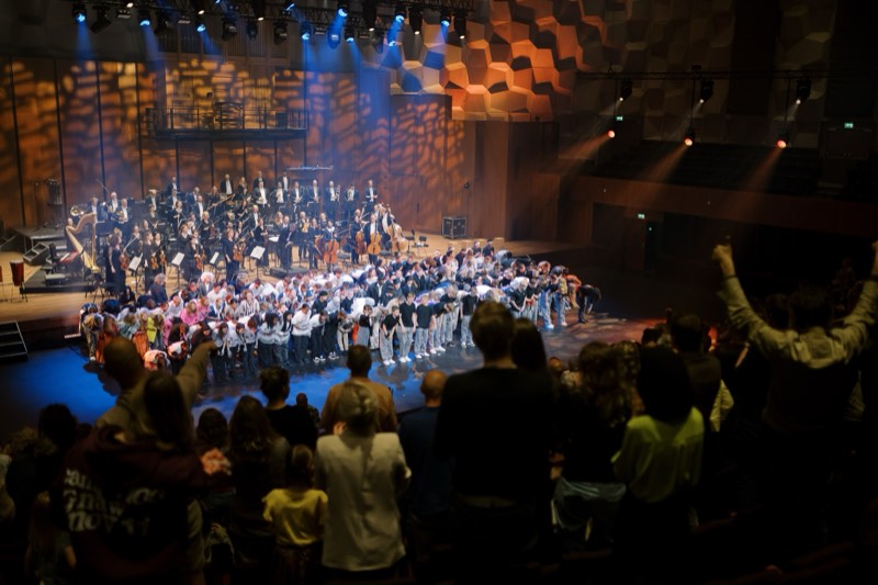 Curtain call from the balcony: several hundred children bowing across the full width of the stage with the orchestra to one side.