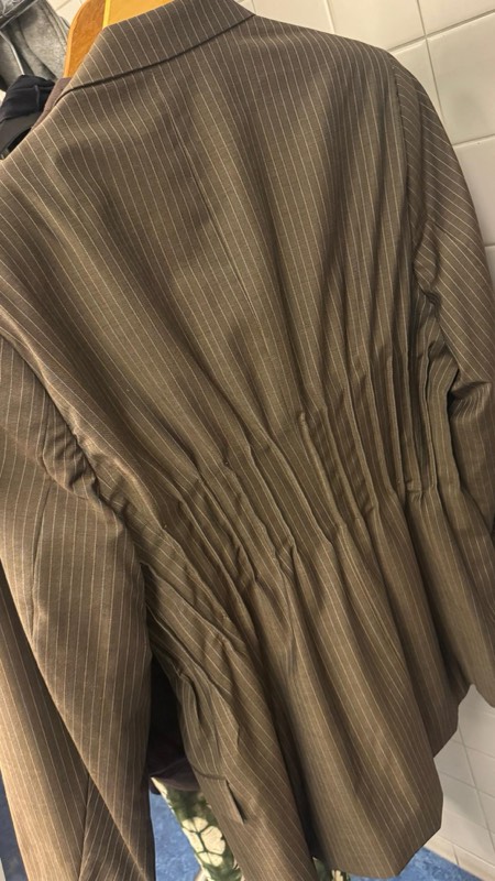 Close view of the back of an olive pinstriped blazer, densely hand shirred across the waist panel.