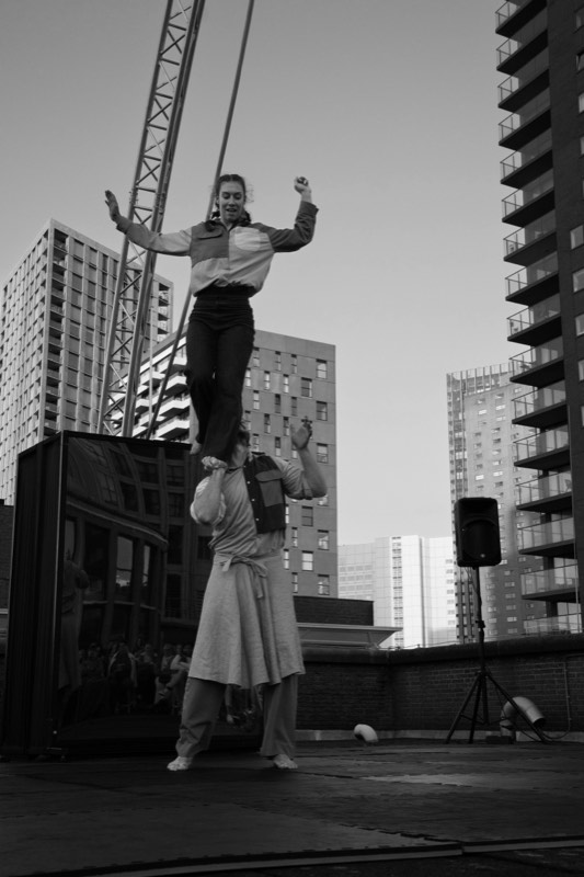 Black and white photograph of an acrobatic duo, one standing on the other hands, in colour-blocked shirts and wrapped apron skirts.