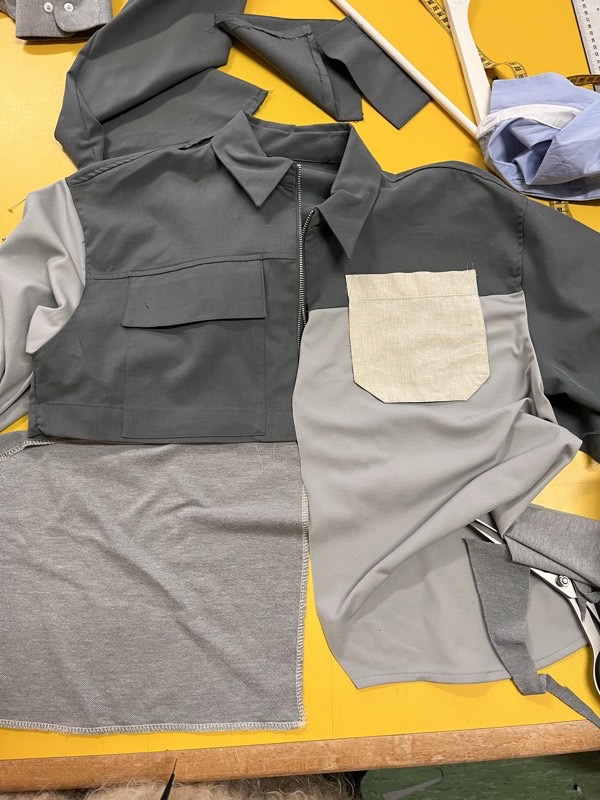 The cut pieces of a colour-blocked grey jacket laid out on a yellow cutting table with shears and a tape measure.